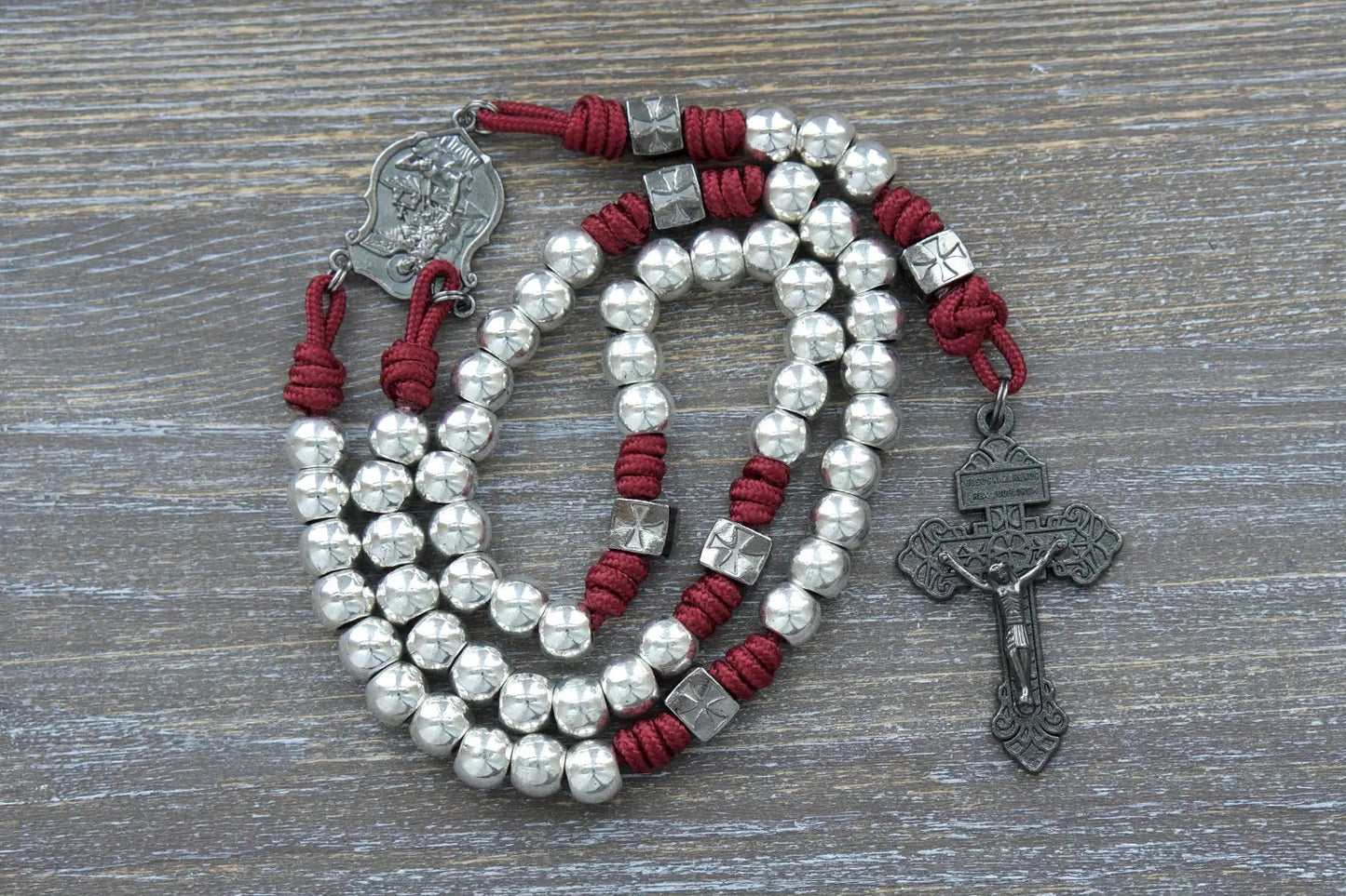 Bold gunmetal rosary with Crimson Red paracord, Hail Mary and Our Father beads, and engraved St. Michael pendant.