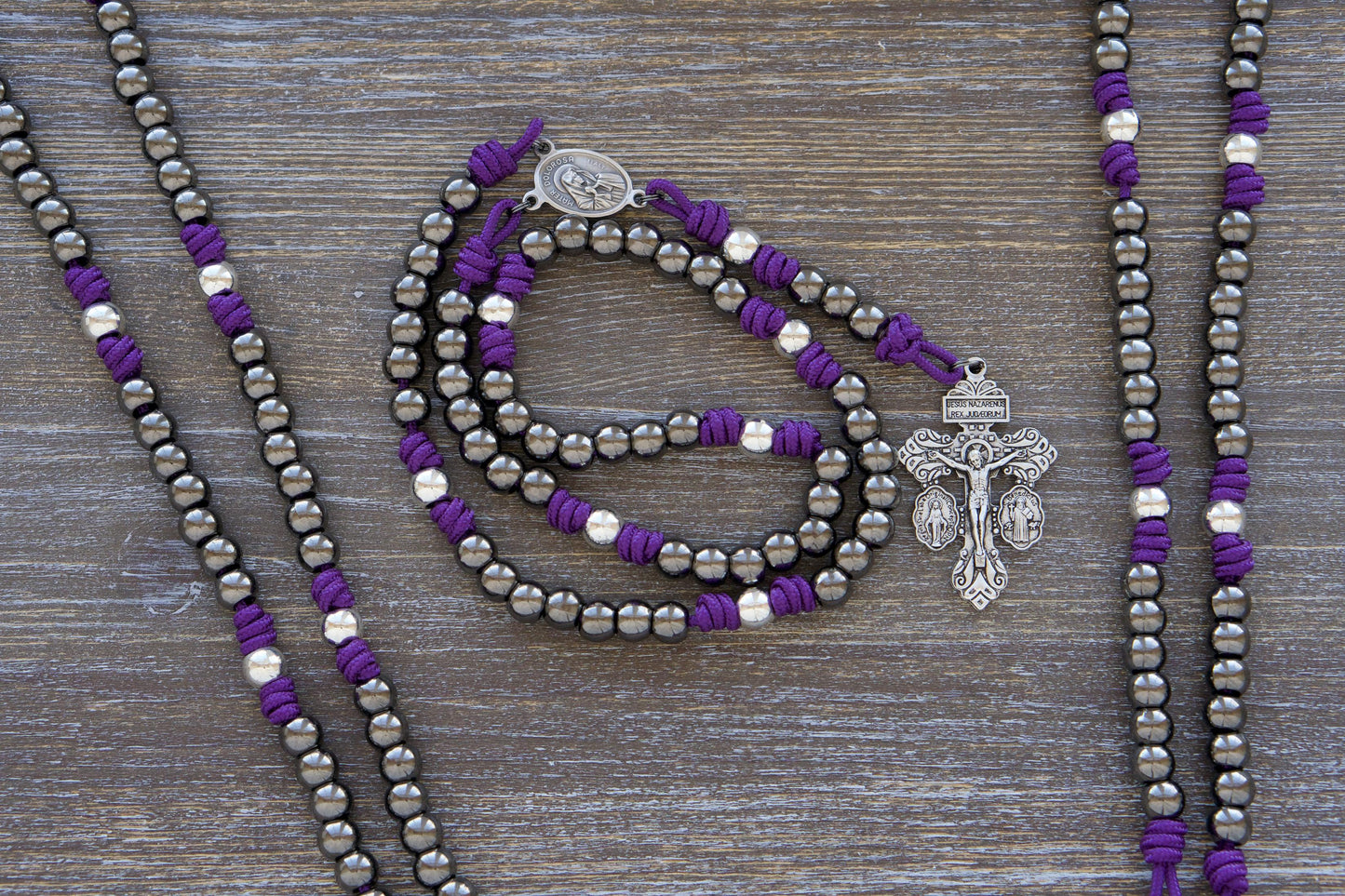 Purple paracord Servite Rosary chaplet featuring 10mm silver Our Father beads, gunmetal Hail Mary beads, and a centerpiece medal with the Mater Dolorosa and Ecce Homo imagery. Includes a robust triple threat pardon crucifix in silver.