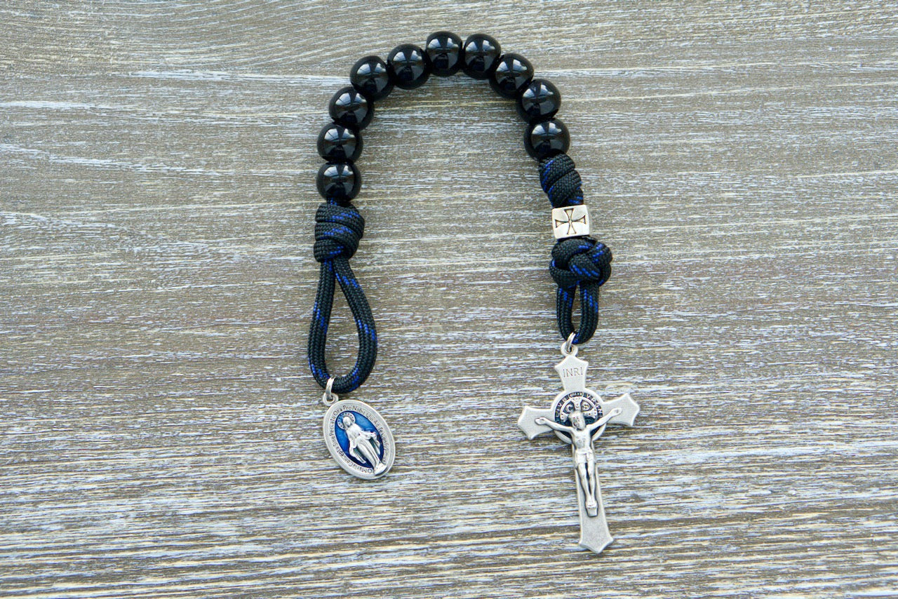 Embrace unwavering devotion with the Solemn Crusader - Blue Black and Silver 1 Decade Paracord Rosary. Handcrafted by our Catholic family for strength, grace, and resilience in faith. Durable paracord, shiny black beads, silver crusader Our Father beads, and a protective St. Benedict crucifix make this rosary an unbreakable spiritual weapon.