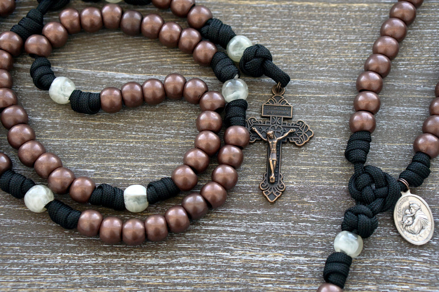St. Anthony, Hammer of Heretics 5 Decade Paracord Rosary in black and copper with pearl beads, featuring a St. Anthony devotional medal and Pardon Crucifix, perfect for daily devotions and prayer.