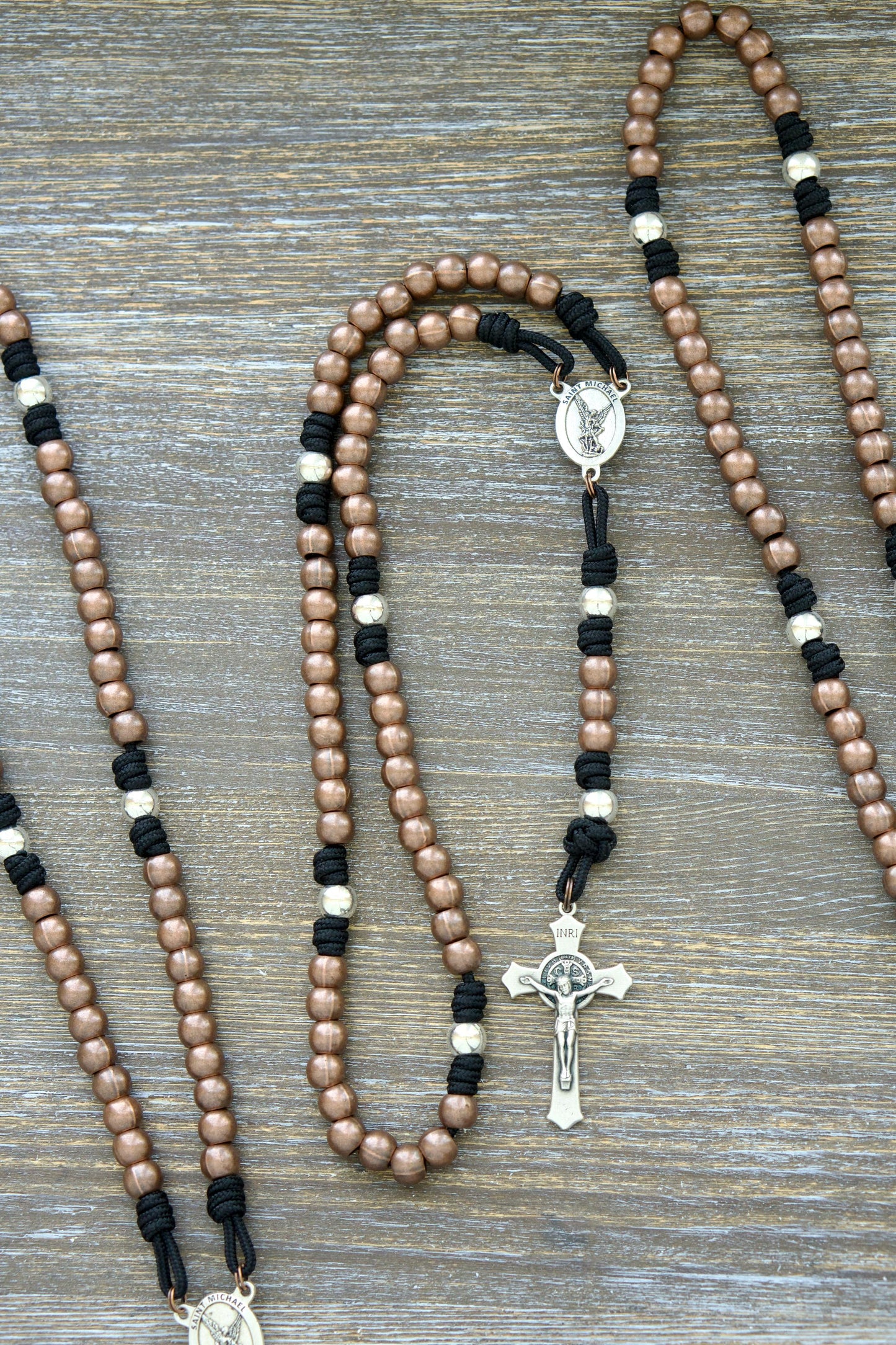 Handcrafted rosary featuring durable paracord (grey, black, green, or navy) with copper Hail Mary beads, silver Our Father beads, a radiant St. Michael centerpiece medal.