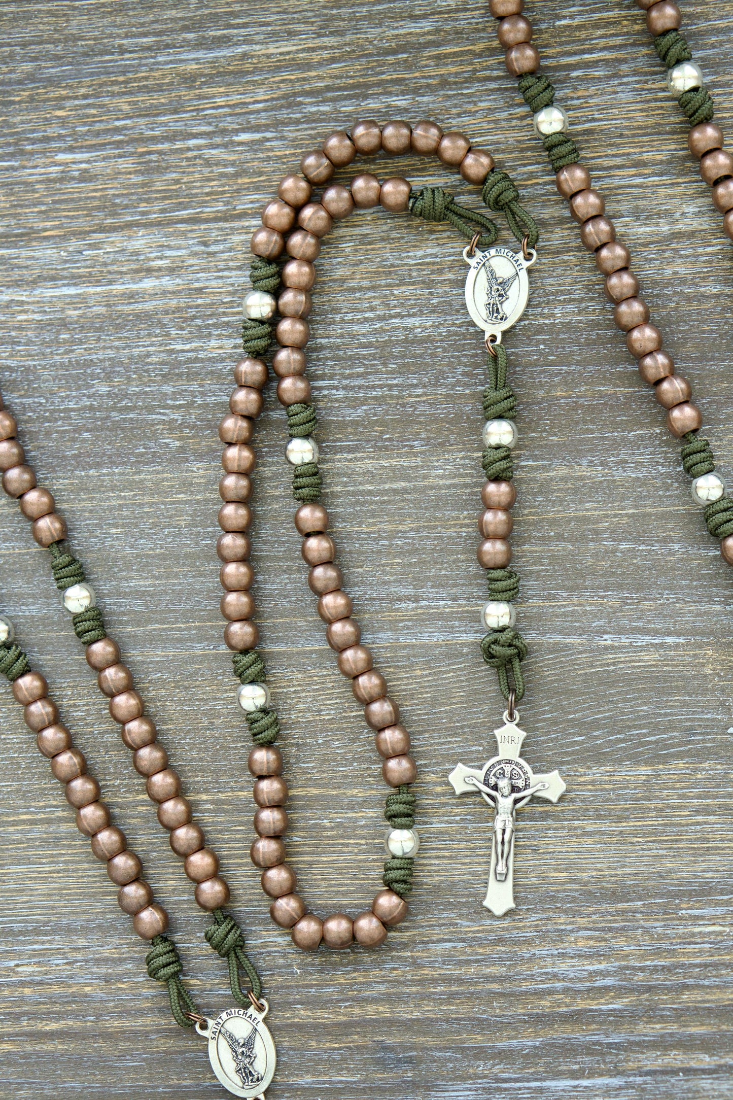 A handcrafted, rugged "St. Michael's Sword" paracord rosary featuring grey, black, green, or navy blue paracord cord, copper Hail Mary beads, silver Our Father beads, a radiant St. Michael centerpiece medal.