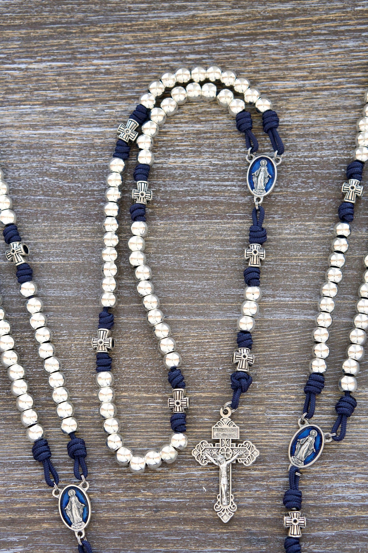 Premium navy blue paracord Rosary, Stella Maris, featuring shiny silver metal alloy Hail Mary beads, cross-shaped Our Father beads, a blue enamel Miraculous Medal centerpiece, and a matching silver 2" Pardon Crucifix.