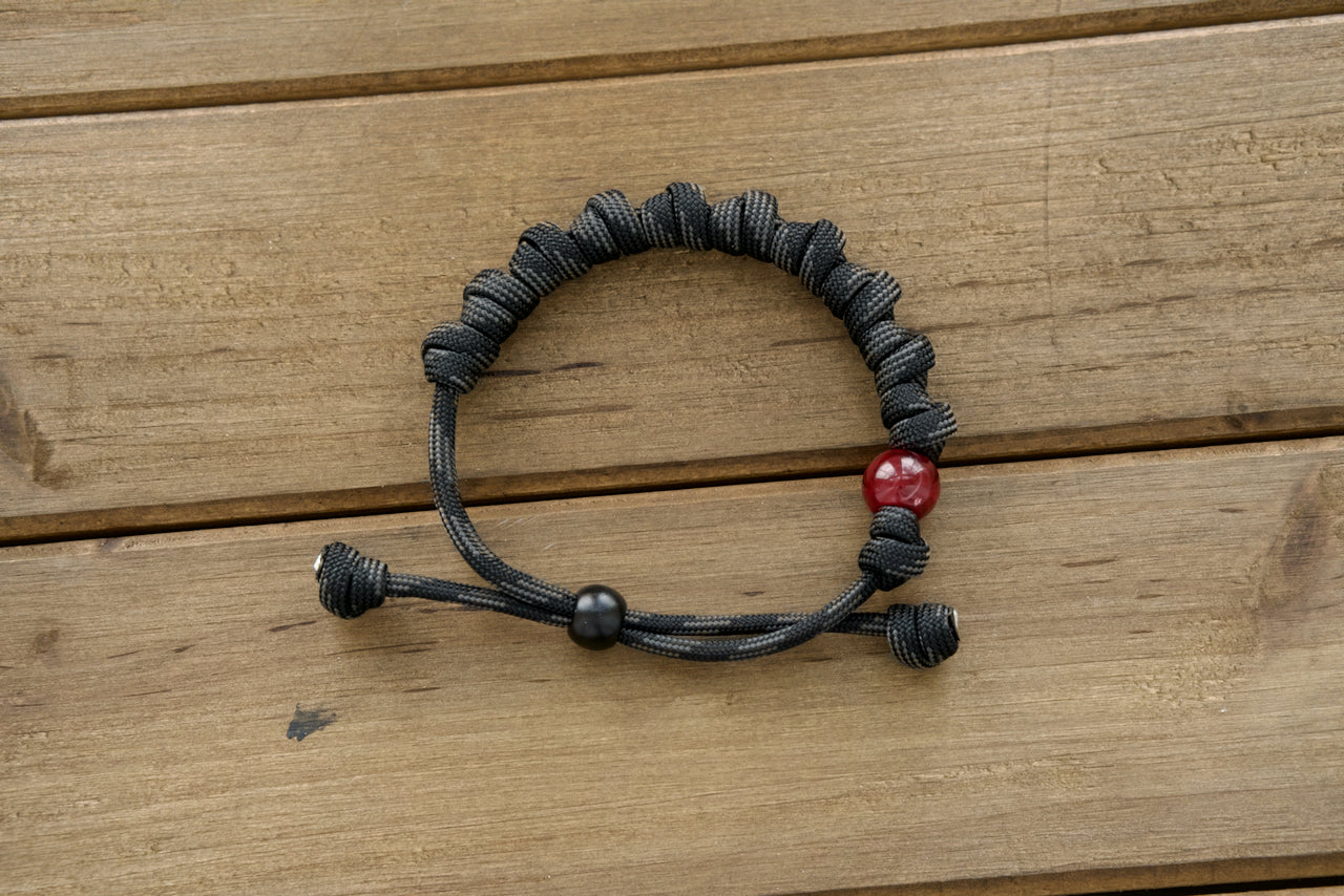 Stunning Terror of Demons - Rosary Bracelet, featuring durable premium black/gray paracord rope, 10 Hail Mary knots, and unique milky red Our Father bead; ideal for daily wear or as a spiritual gift for fellow Catholics.