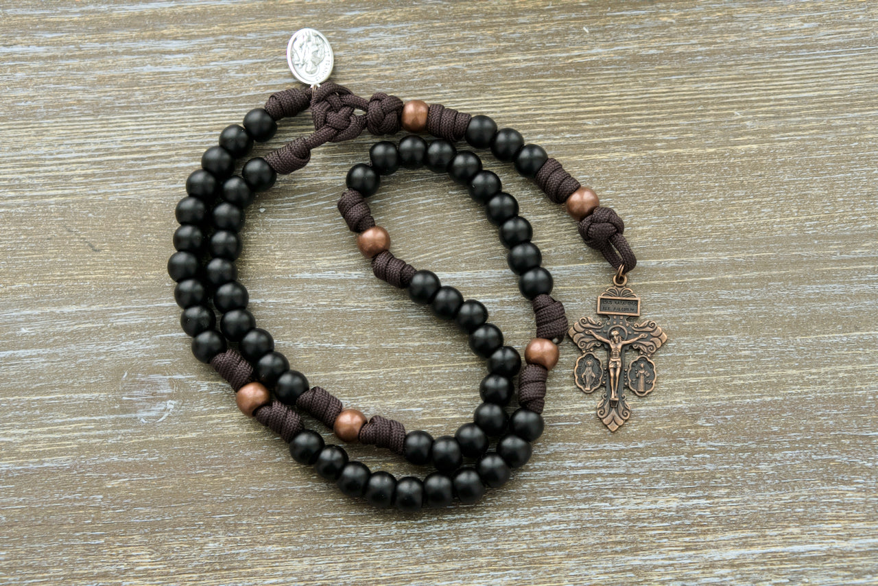 The Franciscan Forge - St. Francis - 5 Decade Paracord Rosary. Handcrafted with premium unbreakable paracord, antique copper Our Father beads, and matte black Hail Mary beads. Featuring a St. Francis devotional medal and a rustic copper 'triple threat' pardon crucifix.