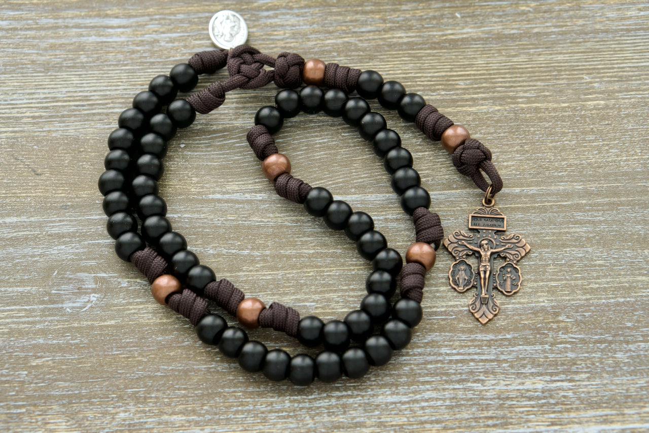 Handcrafted 5 Decade Franciscan Forge Paracord Rosary with antique copper Our Father, matte black Hail Mary beads, and a St. Francis devotional medal; durable, unbreakable, and perfect for strengthening your Catholic faith and spiritual journey.