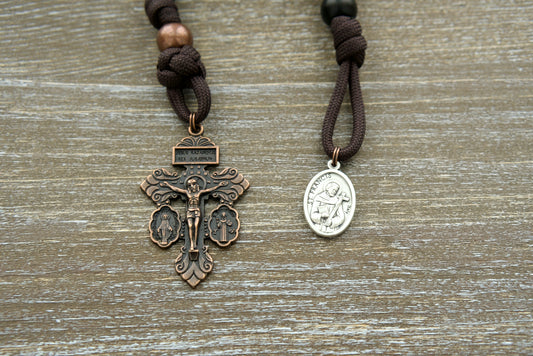 Handcrafted St. Francis Pocket Paracord Rosary, featuring durable brown paracord, matte black Hail Mary beads, copper Our Father beads, St. Francis devotional medal, and a 2-inch Triple Threat Pardon Crucifix.