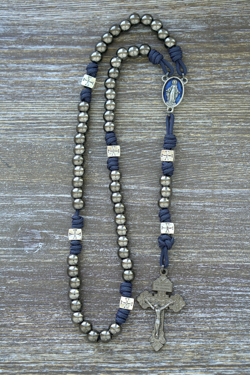 Premium navy blue paracord rosary, "The Solemn Crusader," featuring silver crusader Our Father beads, gunmetal Hail Mary beads, a Miraculous Medal centerpiece, and a 2-inch pardon crucifix.