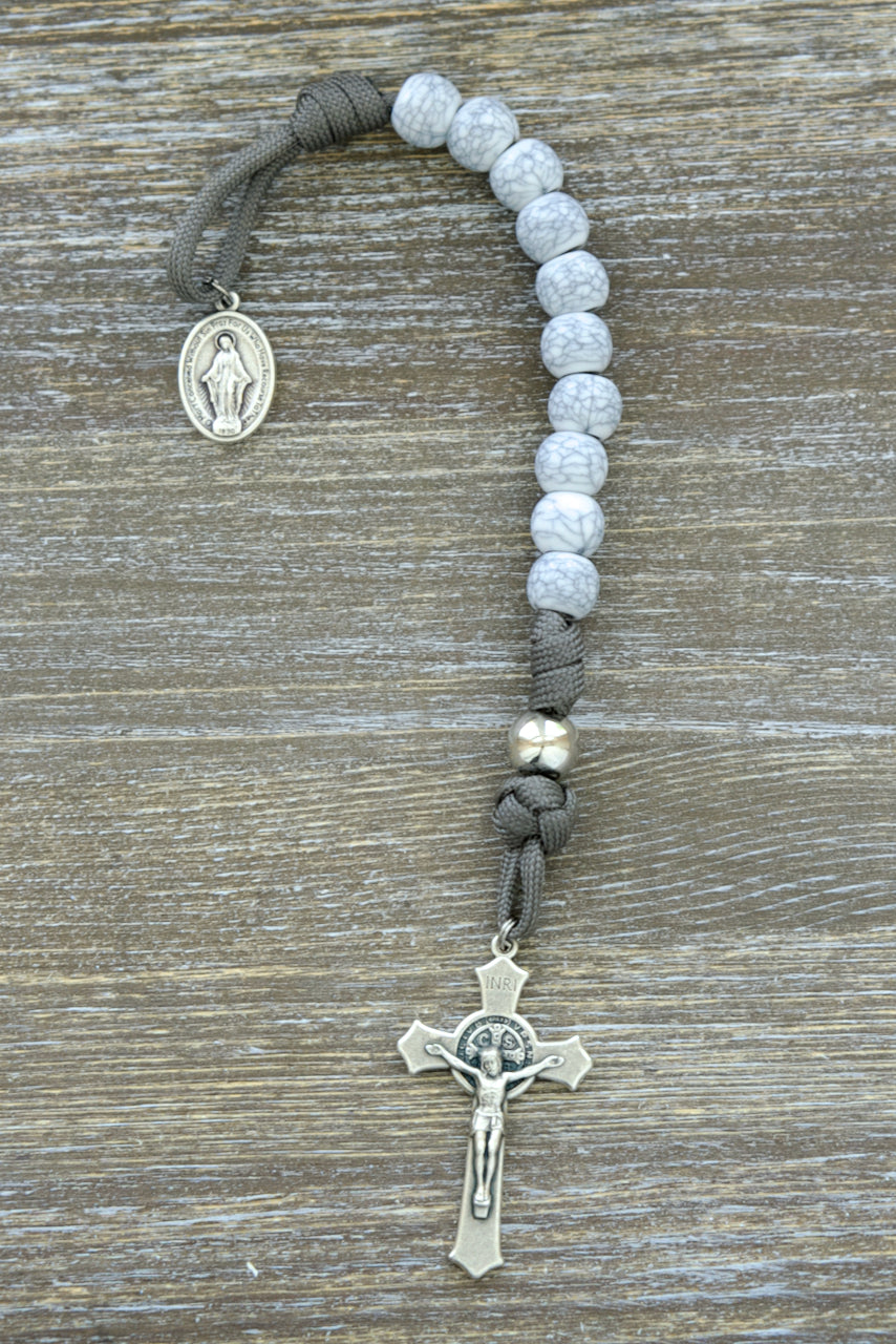 Premium unbreakable paracord rosary featuring unique cracked ivory looking Hail Mary beads, dark grey rope, and silver Our Father beads; includes a Miraculous Medal devotional medal and a 2-inch St. Benedict Crucifix for added protection on your Catholic faith journey.