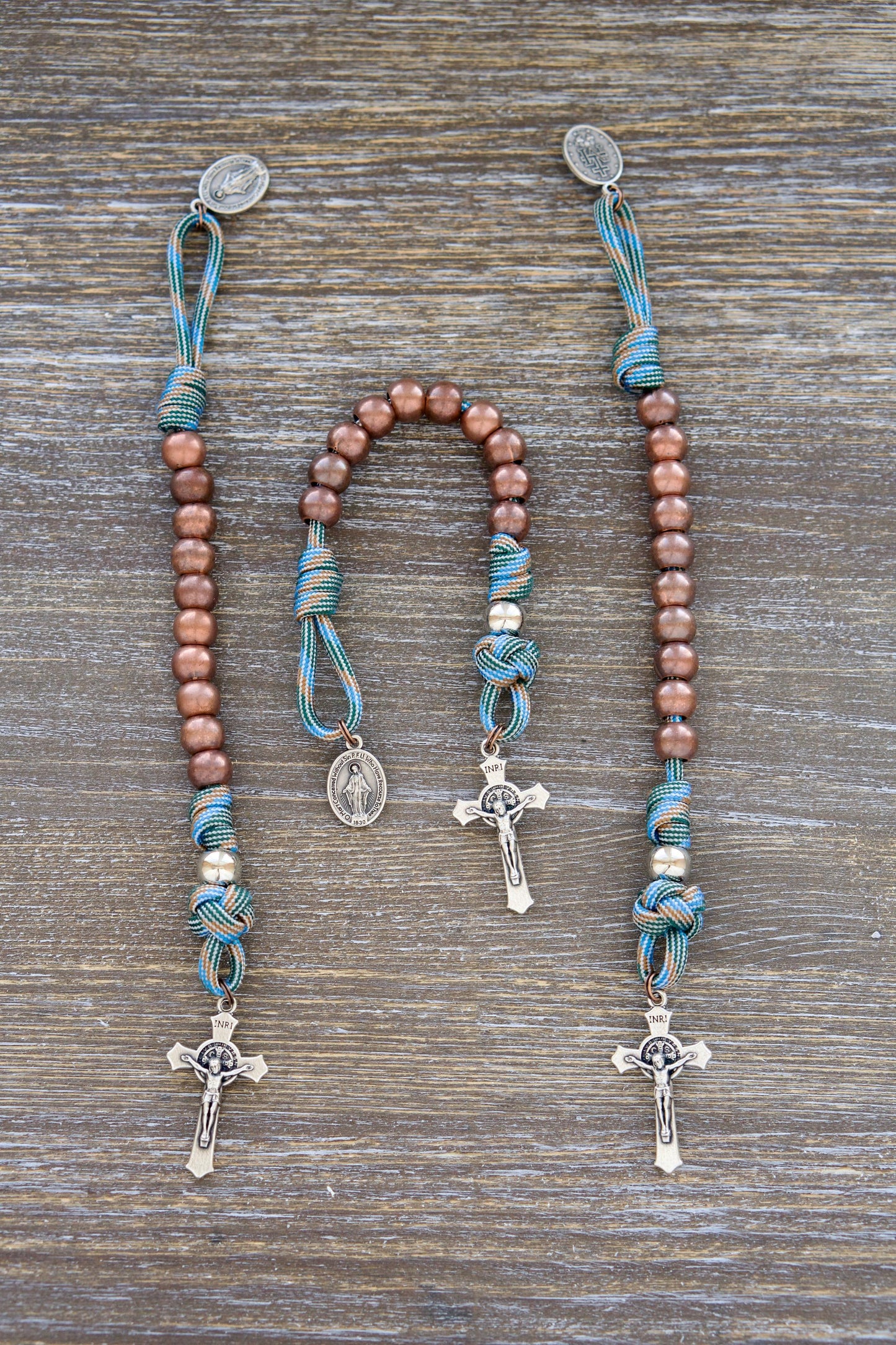 A vibrant light blue and brown paracord rosary designed for kids, featuring 10mm antique copper Hail Mary beads, 10mm shiny silver Our Father beads, and a small Miraculous Medal crucifix. Perfect for young Catholic adventurers.