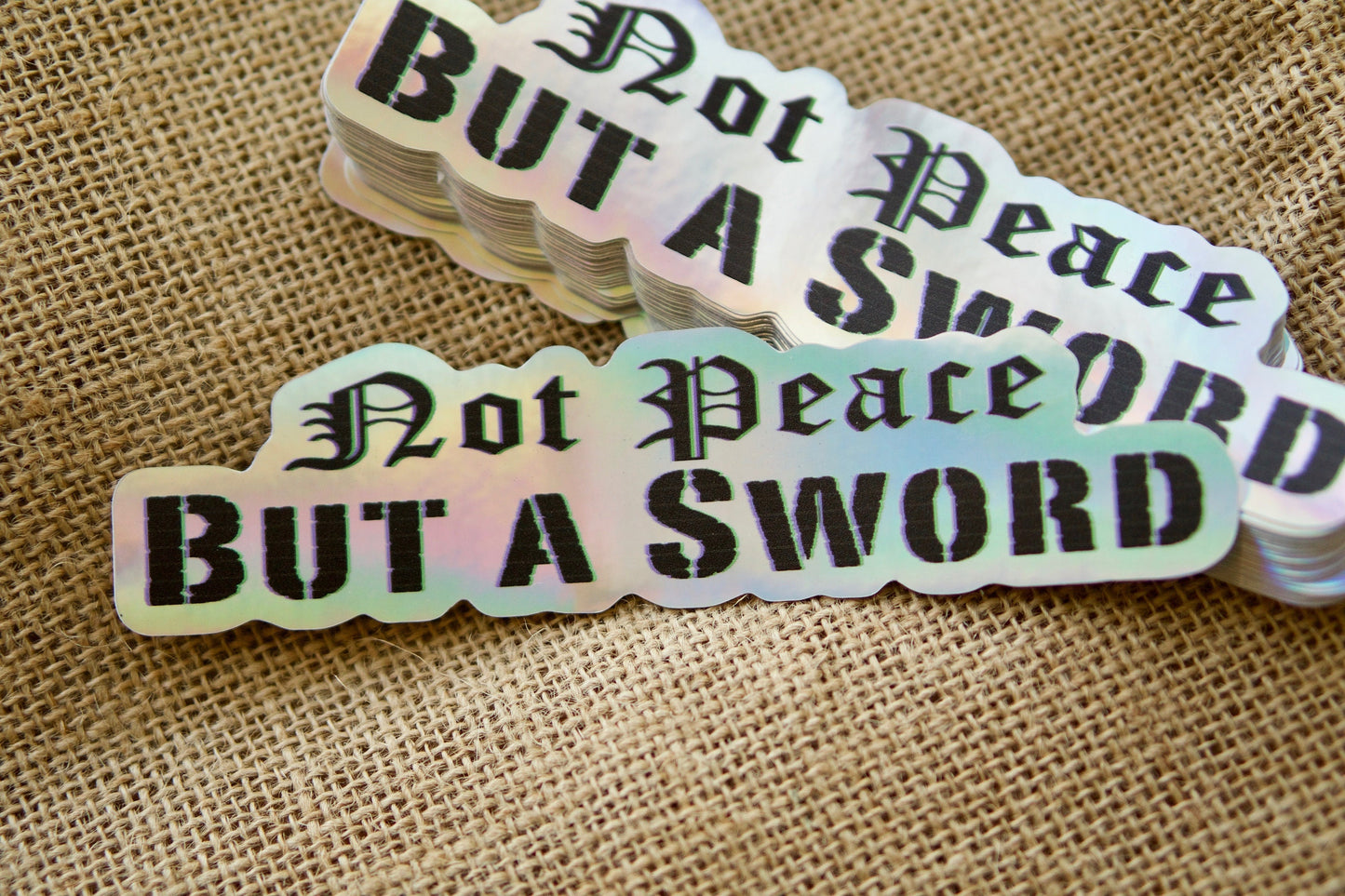 Not Peace but a Sword - Holographic Vinyl Sticker (6" x 1.5") for laptops and water bottles, reminding us of Matthew 10:34; also available in regular white (5" x 1"). Perfect Catholic gift to pair with your paracord rosary.