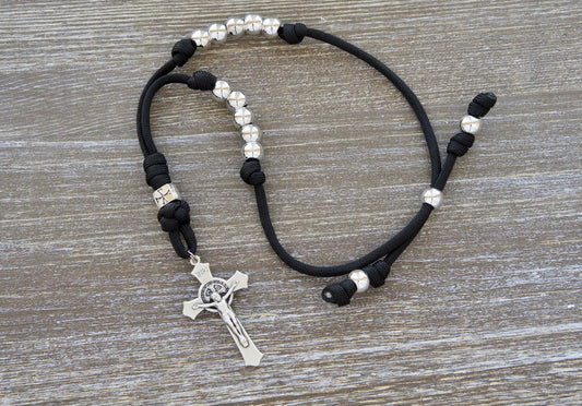 Black and silver paracord rosary with 10 Hail Mary beads and a metal crusader Our Father bead, hanging from a standard size 2" St. Benedict crucifix on a rearview mirror.