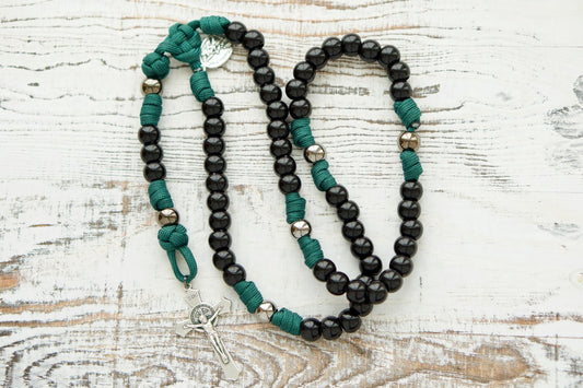 A beautifully crafted Dark Night of the Soul 5 Decade Paracord Rosary, featuring dark green rope and black & gunmetal beads for a sleek and powerful design. The St. Michael and Guardian Angel devotional medal offer protection while the St. Benedict Crucifix serves as a reminder of Christ's sacrifice and protection.