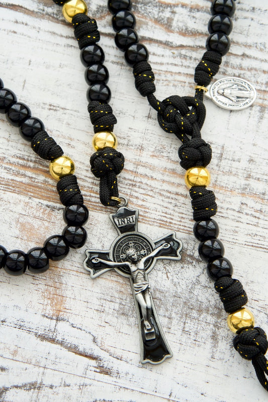 The Holy Servant - Black and Gold - 5 Decade Paracord Rosary: A sophisticated and elegant Catholic gift, featuring black paracord with gold ribbon interwoven, luxurious gold Our Father beads, shiny black Hail Mary beads, a large black enamel crucifix, and a miraculous medal. Perfect for personal prayer or as a meaningful present.