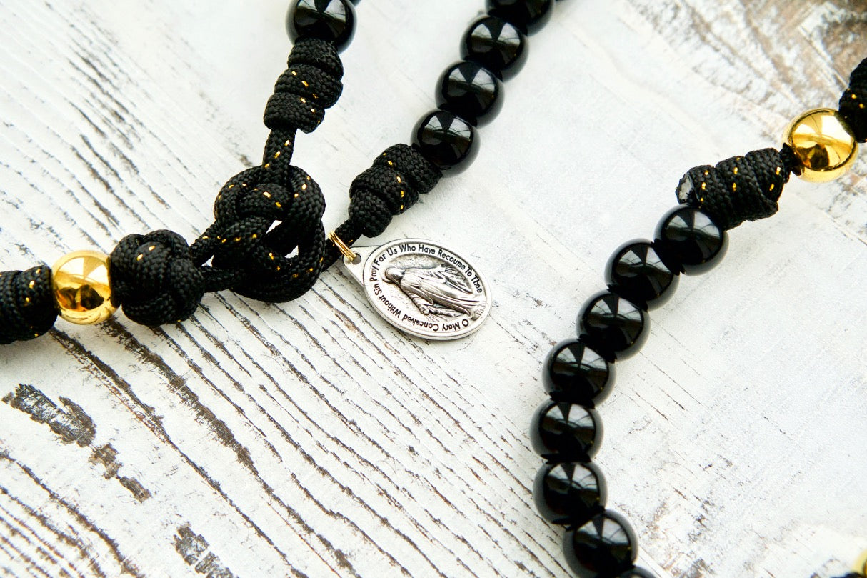 The Holy Servant - Black and Gold - 5 Decade Paracord Rosary: Elegant, devotional rosary with black paracord, gold ribbon, shiny black Hail Mary beads, golden Our Father beads, large black enamel crucifix, and miraculous medal. Perfect for prayer practice or as a meaningful gift.
