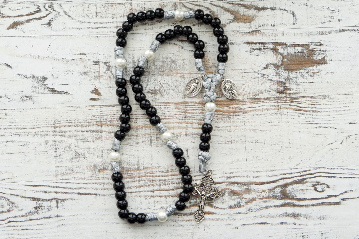 Mater Dolorosa - Our Lady of Sorrows - 7 Sorrows Paracord Rosary, featuring a powerful design with black, grey, and white colors, handmade by a small Catholic family of 6, guaranteed to never break or fail in battle. Includes a silver 2" Pardon Crucifix and Miraculous Medal paired with a Mater Dolorosa/Ecce Homo medal.