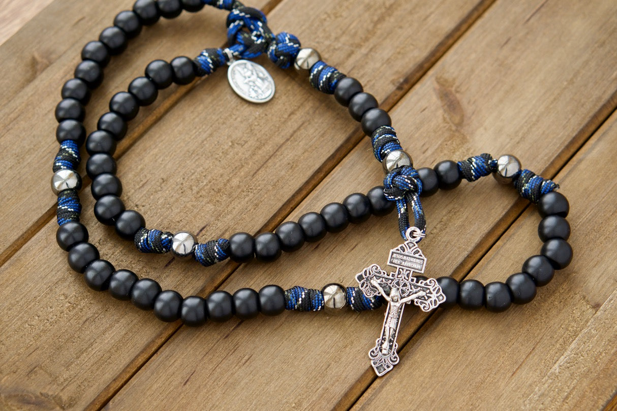 Embrace divine protection with our Thin Blue Line - 5 Decade Paracord Rosary. This premium unbreakable paracord rosary combines stylish thin blue line camo rope, matte black Hail Mary beads, gunmetal Our Father beads, Pardon Crucifix, and devotional medal featuring St. Michael & Guardian Angel for a powerful Catholic gift.