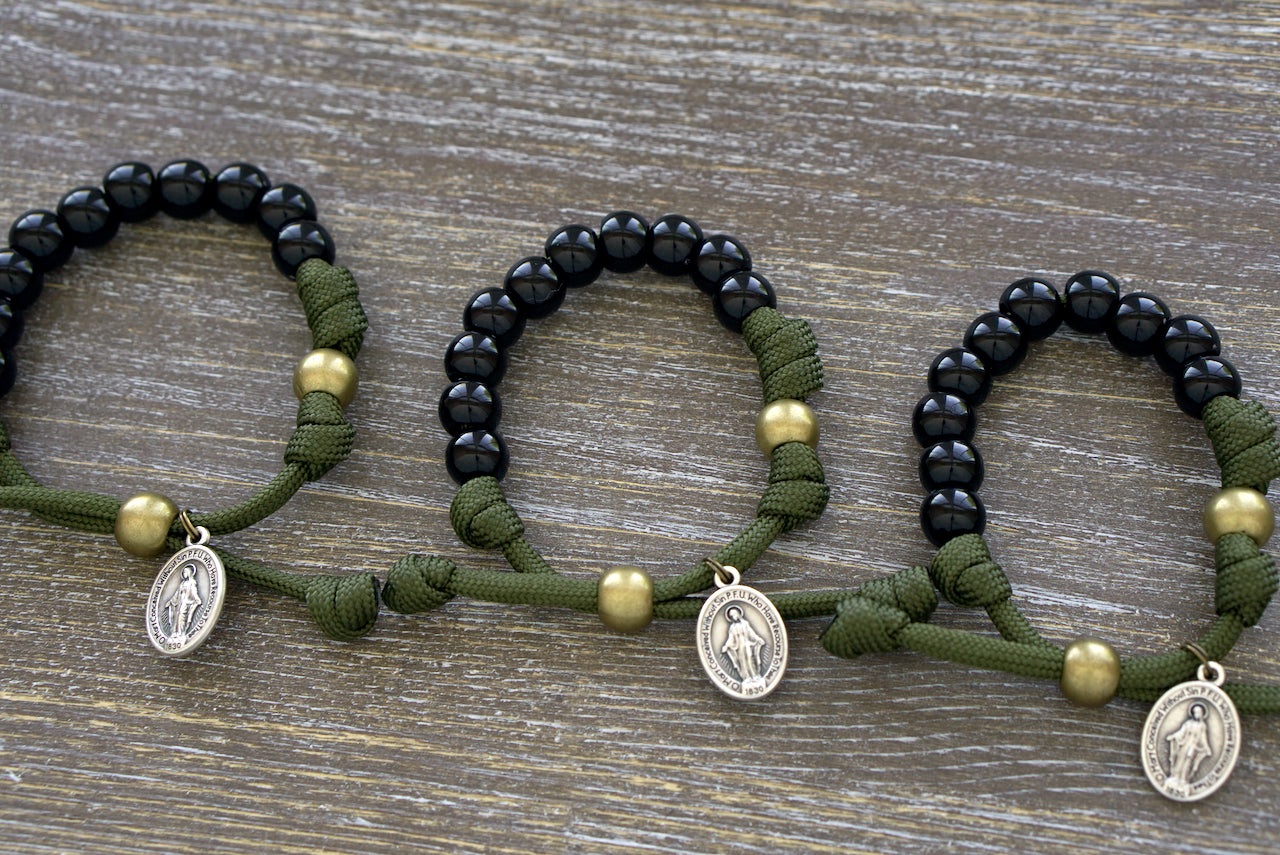 Army Green and Black Kid's Rosary Bracelet featuring durable paracord, black acrylic beads for Hail Mary prayers, olive Our Father bead, and a Miraculous Medal. 