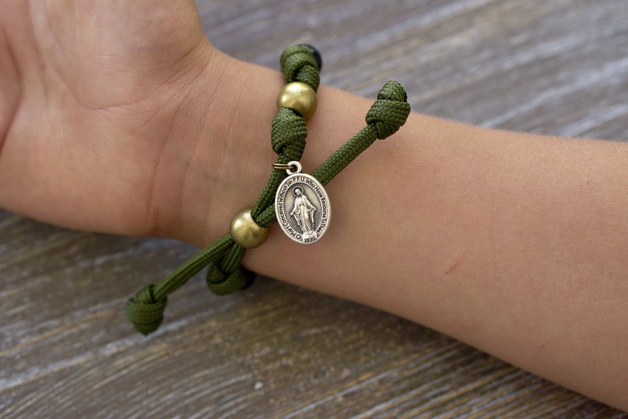 Army Green and Black Kid's Rosary Bracelet, featuring an eye-catching paracord design with black beads symbolizing Hail Mary prayers, olive Our Father bead, and a small Miraculous Medal for young Catholics.