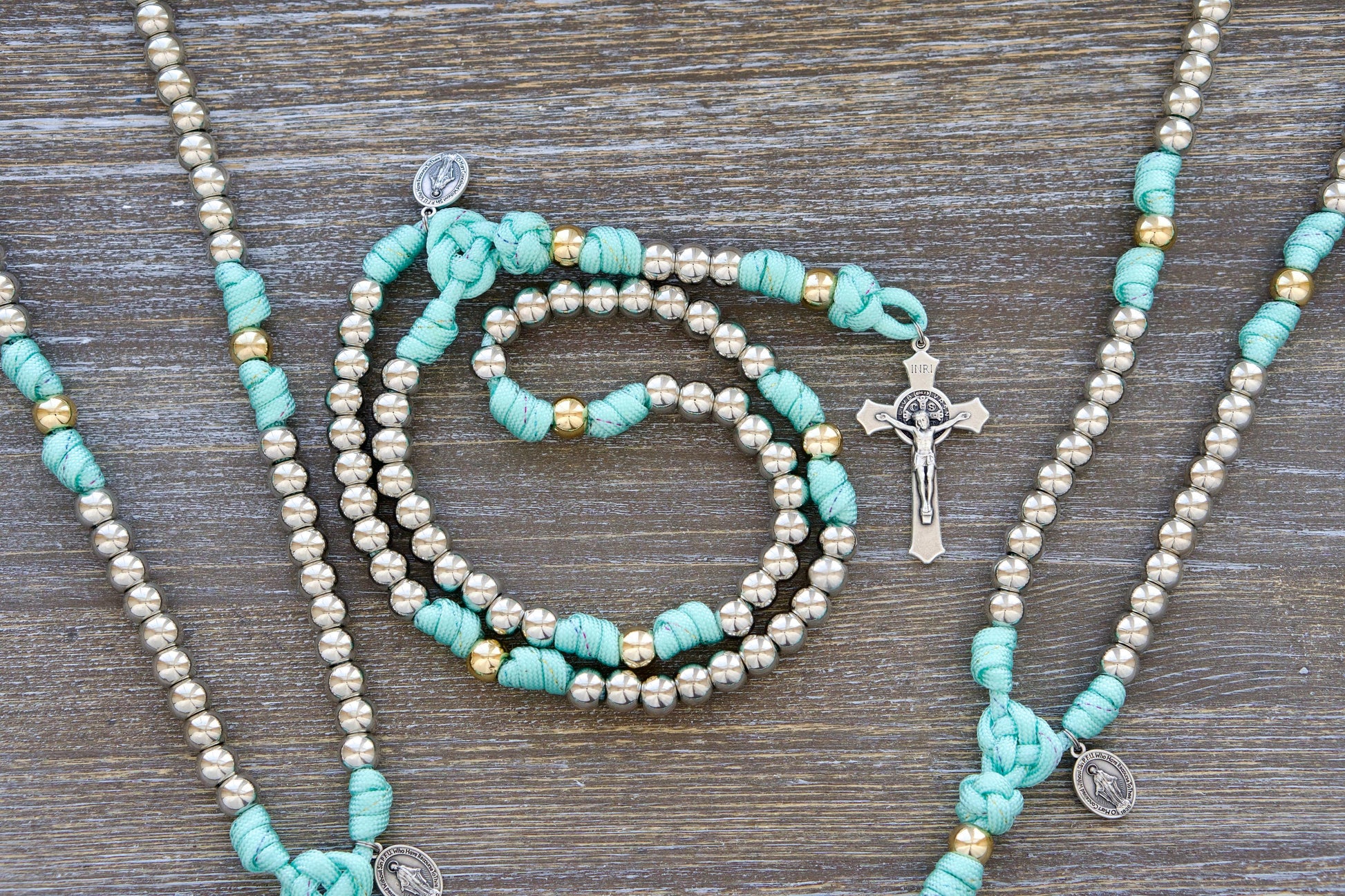 August Queen of the Heavens Kid's Rosary: A teal blue and rainbow paracord rosary with 10mm silver and gold acrylic beads, featuring a 2-inch St. Benedict crucifix and a 3/4-inch Miraculous Medal.