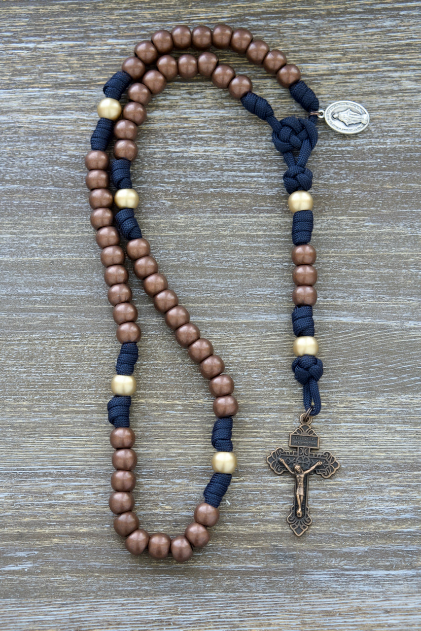 Beautifully crafted, 5 decade paracord rosary with navy blue and antique copper accents, featuring a 2-inch copper Pardon Crucifix and Miraculous Medal. Unbreakable Catholic gift for devotion and strength.