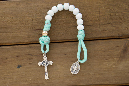 Kid's mint green paracord pocket rosary with white Hail Mary and rose gold Our Father beads, featuring a smaller St. Benedict Crucifix and Miraculous Medal, perfect for First Communion or Easter gifts.