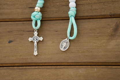 Kid's mint green paracord pocket rosary with white Hail Mary and rose gold Our Father beads, featuring a smaller St. Benedict Crucifix and Miraculous Medal. Perfect for First Communion or Easter gifts for children.