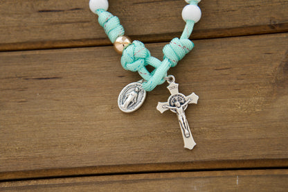 Kid's mint green paracord pocket rosary with white Hail Mary beads and rose gold Our Father beads, featuring a smaller St. Benedict Crucifix and Miraculous Medal, ideal for First Communion or Easter gifts.