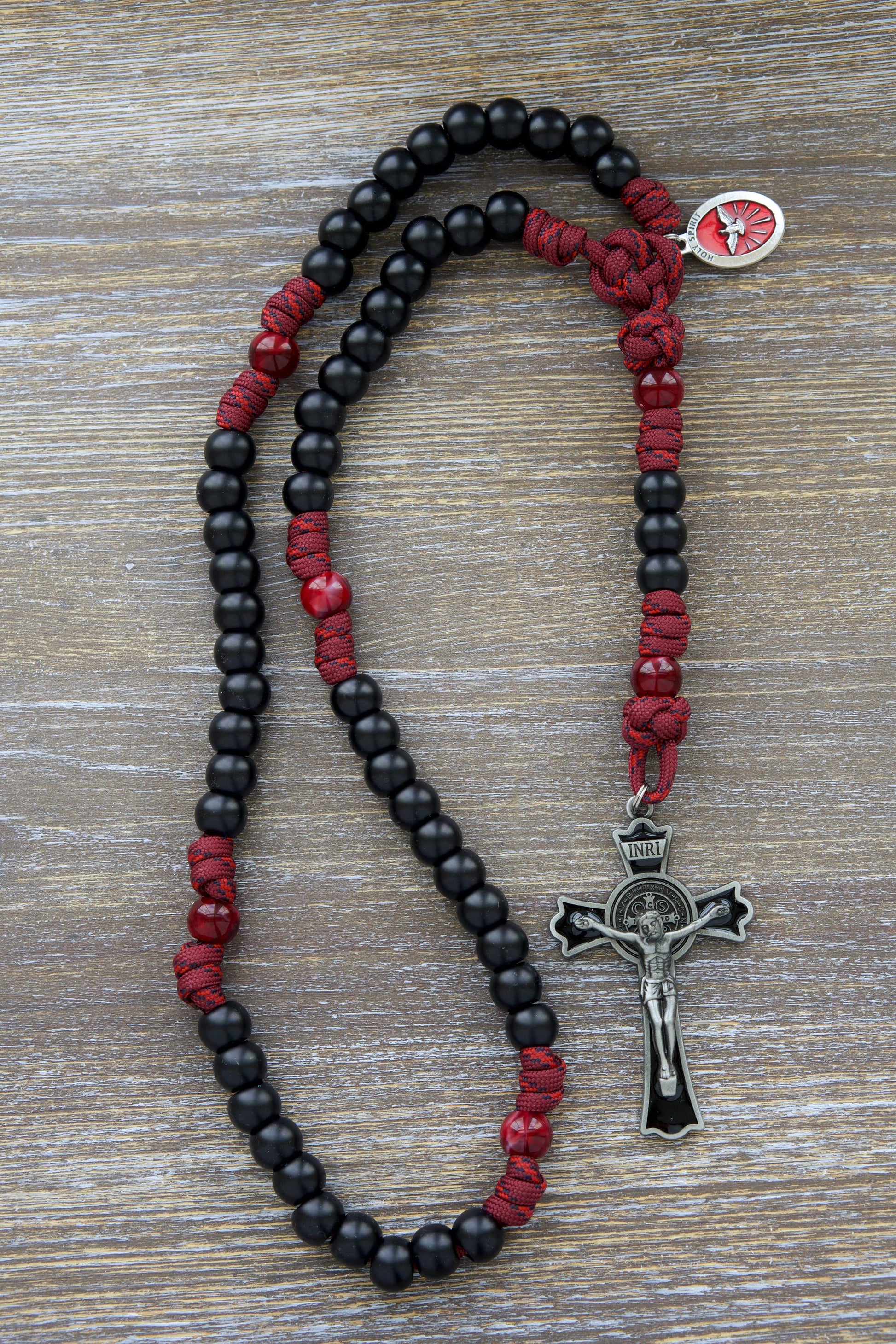 Crimson Shield Rosary: A handcrafted 5-decade paracord rosary in maroon red, featuring black or white Hail Mary beads, a gleaming black (or white) enamel St. Benedict crucifix, and a vibrant red Holy Spirit devotional medal.