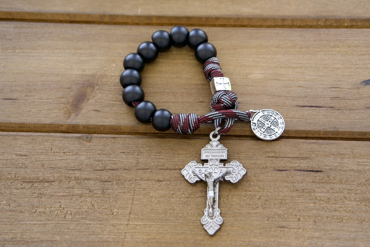 The Crusader Pocket Paracord Rosary - DEUS VULT! This handmade, premium-quality 1 Decade Pocket Paracord Rosary features 12mm acrylic Hail Mary beads in matte black and a metal alloy silver crusader Our Father bead. Its durable red and silver paracord ensures it can withstand any challenge, while the St. Benedict devotional medal offers added protection.