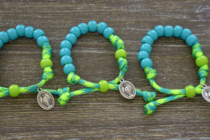 David's Slingshot Kids Rosary Bracelet in Lime Green and Sky Blue, featuring 10mm blue beads for Hail Mary prayers and a matching lime green Our Father bead, along with a petite Miraculous Medal on paracord.