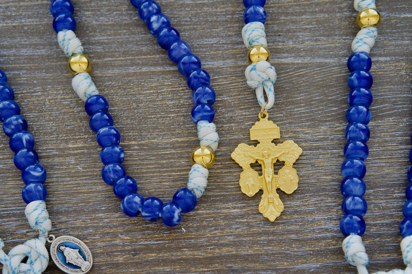 Handcrafted Divine Light 5 Decade Rosary featuring white paracord, blue accents, luminous 12mm gold Our Father beads, exclusive Miraculous Blue acrylic Hail Mary beads, a blue enamel Miraculous Medal, and a gold Triple Threat Pardon crucifix.