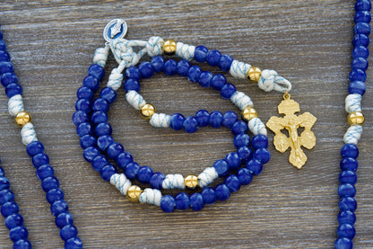  5 Decade Paracord Rosary: White paracord infused with blue accents, featuring radiant gold Our Father beads, unique blue acrylic Hail Mary beads, and a blue enamel Miraculous Medal.  A striking gold crucifix completes this luminous rosary, ideal for prayer and spiritual devotion.