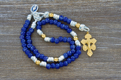 White paracord rosary with blue accents, featuring radiant gold Our Father beads, custom "Miraculous Blue" acrylic Hail Mary beads, and a blue enamel Miraculous Medal and gold triple threat pardon crucifix.  Depicts the Divine Light 5-decade Rosary by Sanctus Servo.