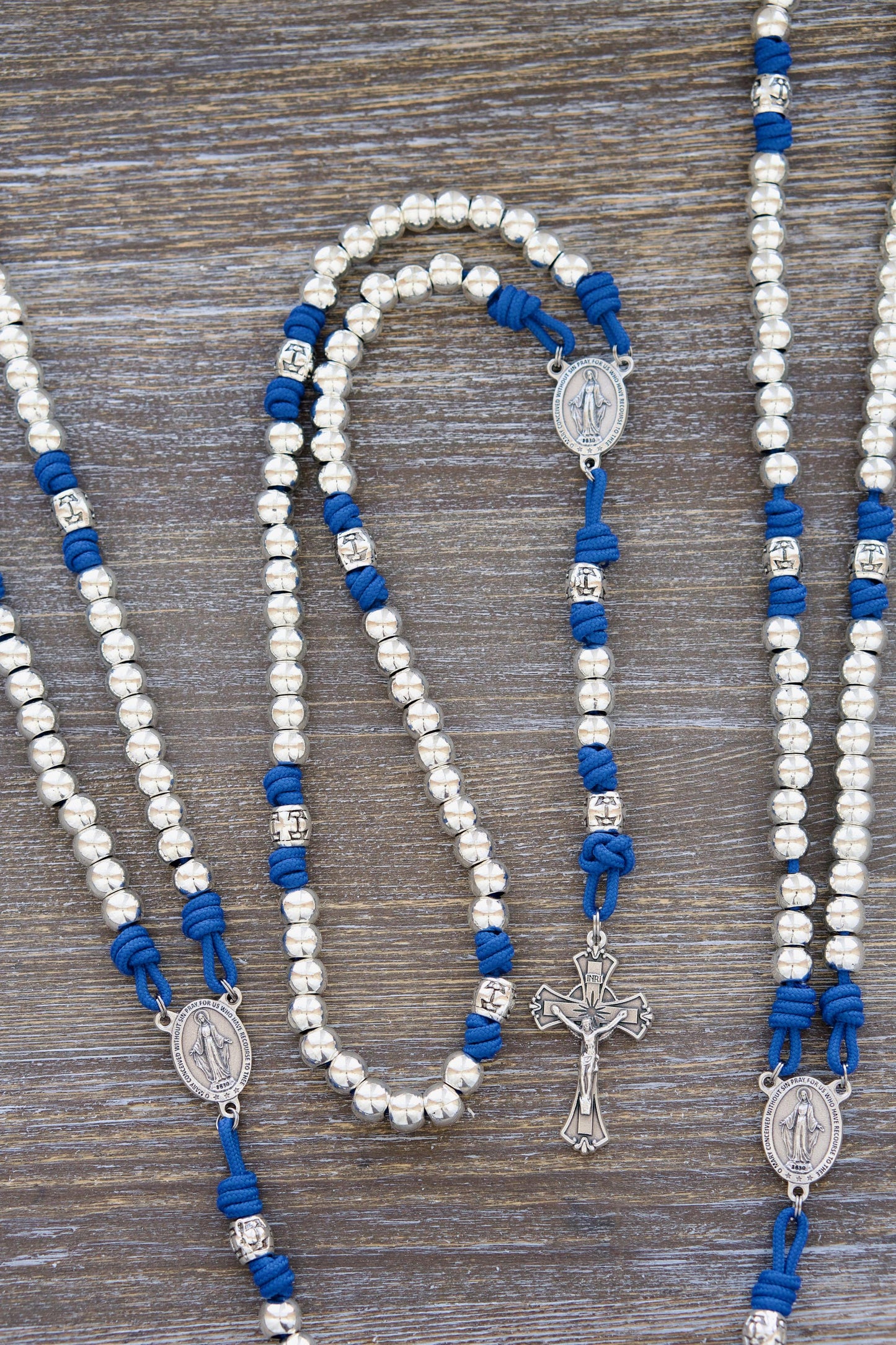 Divine Radiance Premium Metal Paracord Rosary: A handcrafted rosary featuring luminous 'miraculous blue' paracord, gleaming silver metal Hail Mary beads (10mm), a distinctive silver cross barrel design, and a centerpiece Miraculous Medal and Crucifix.