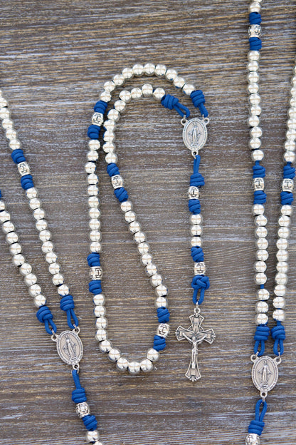 Divine Radiance Premium Metal Paracord Rosary: A handcrafted rosary featuring luminous 'miraculous blue' paracord, gleaming silver metal Hail Mary beads (10mm), a distinctive silver cross barrel design, and a centerpiece Miraculous Medal and Crucifix.