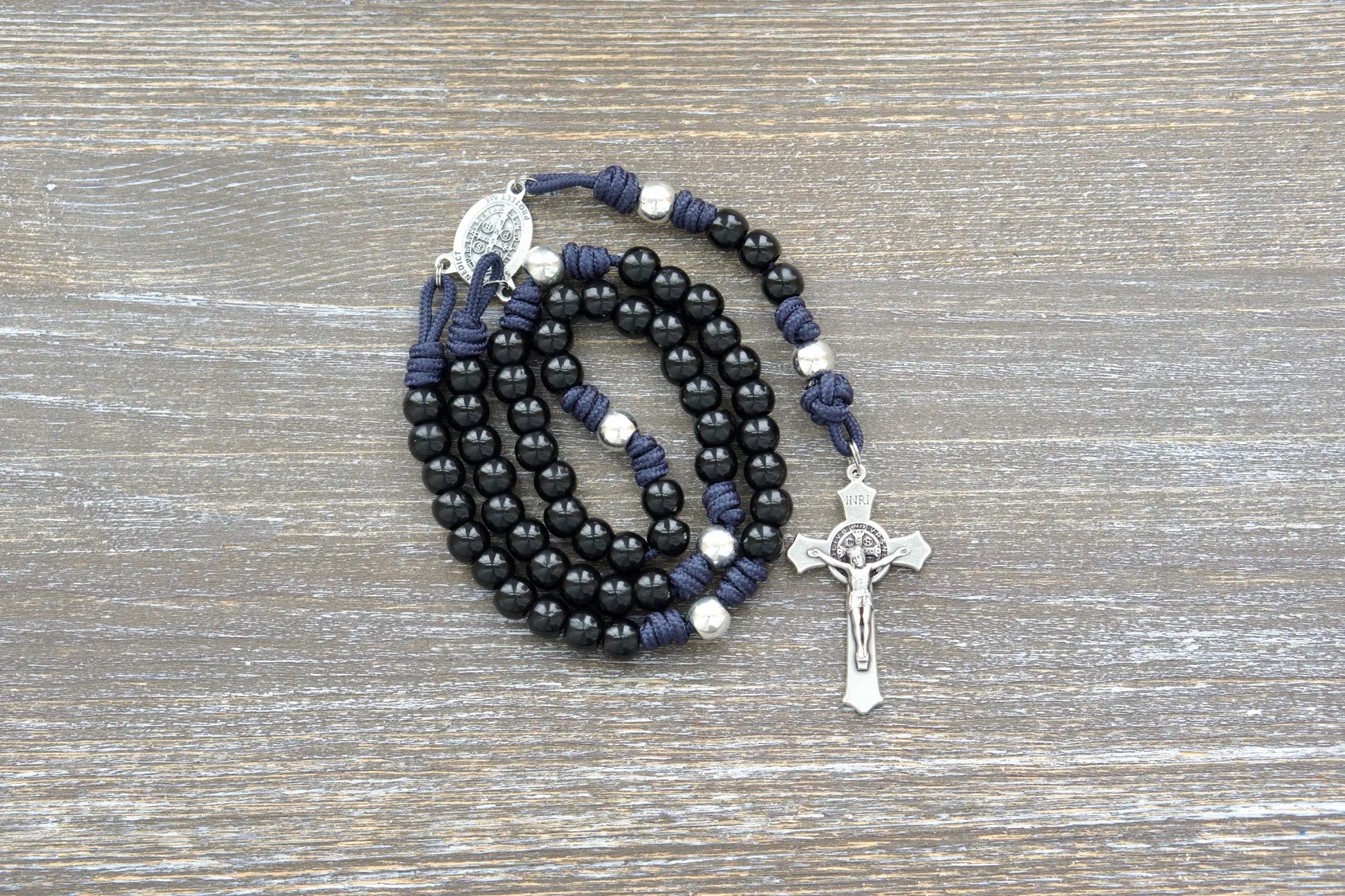 Sturdy navy blue paracord rosary with contrasting silver Our Father beads and black Hail Mary beads, featuring a St. Benedict medal centerpiece and crucifix.
