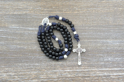 Sturdy navy blue paracord rosary with contrasting silver Our Father beads and black Hail Mary beads, featuring a St. Benedict medal centerpiece and crucifix.
