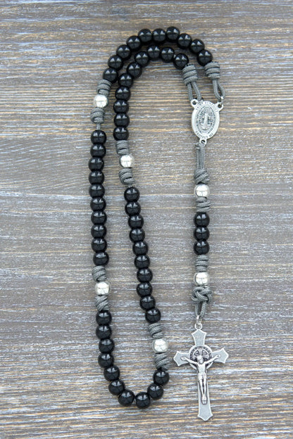 Silver Our Father beads accented by black metal Hail Mary beads on an iron gray paracord rosary with a St. Benedict crucifix.  