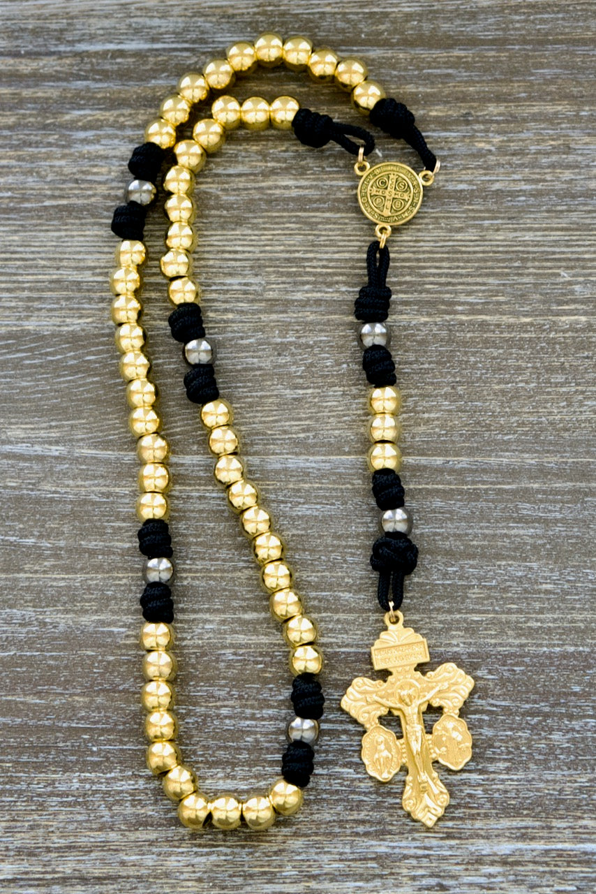 Faith and Valor | Metal Premium Paracord Rosary with Gold, Gunmetal and Black Aesthetic. Exquisitely crafted St. Benedict center devotional medal and 2-inch 'Triple Threat' Pardon crucifix adorn this durable metal rosary featuring 10mm gold Hail Mary beads and gunmetal Our Father beads.