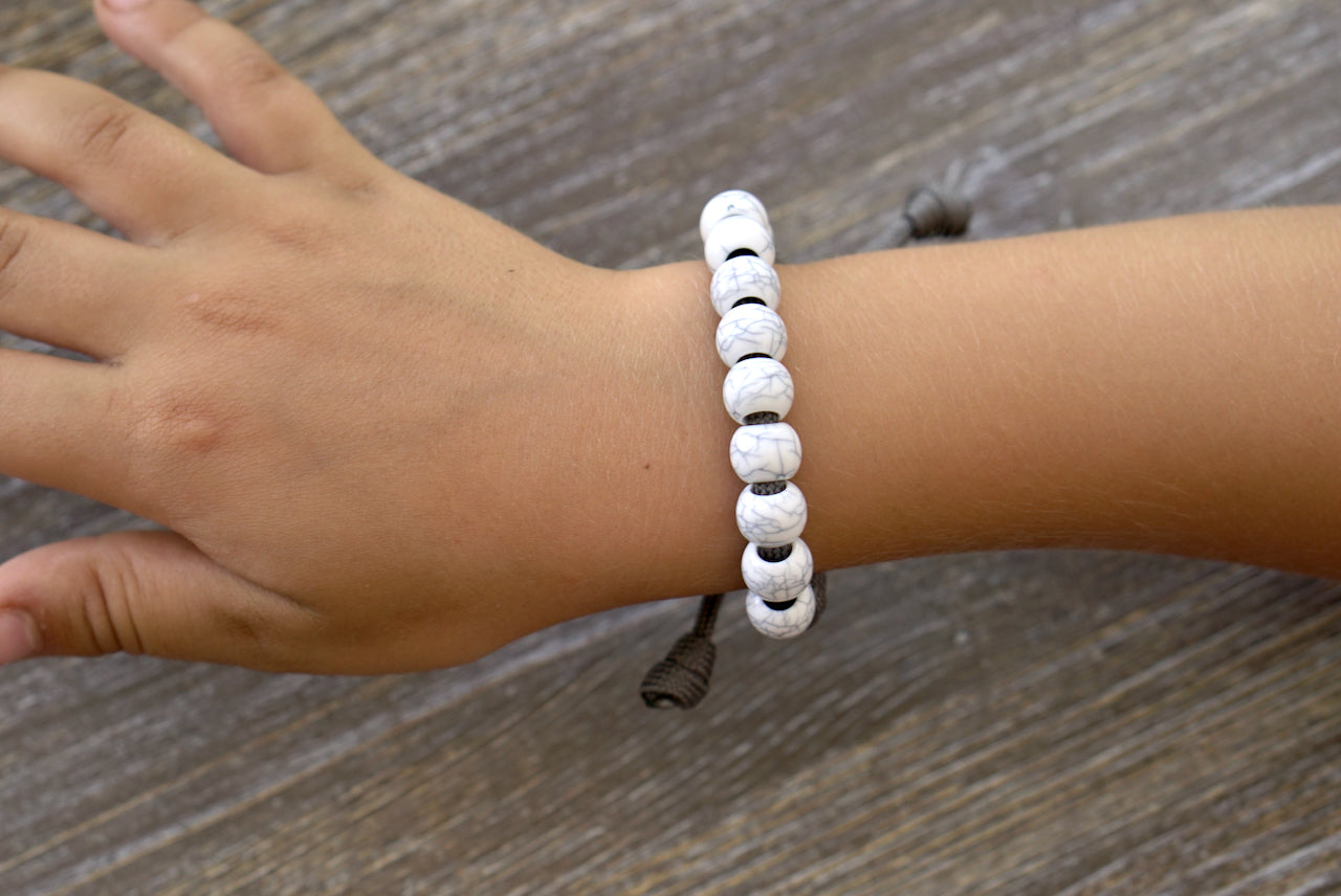 Faithful Fortress Kid's Rosary Bracelet featuring dark grey paracord rope, small 'cracked ivory' Hail Mary beads, silver Our Father bead, and a miniature Miraculous Medal. 