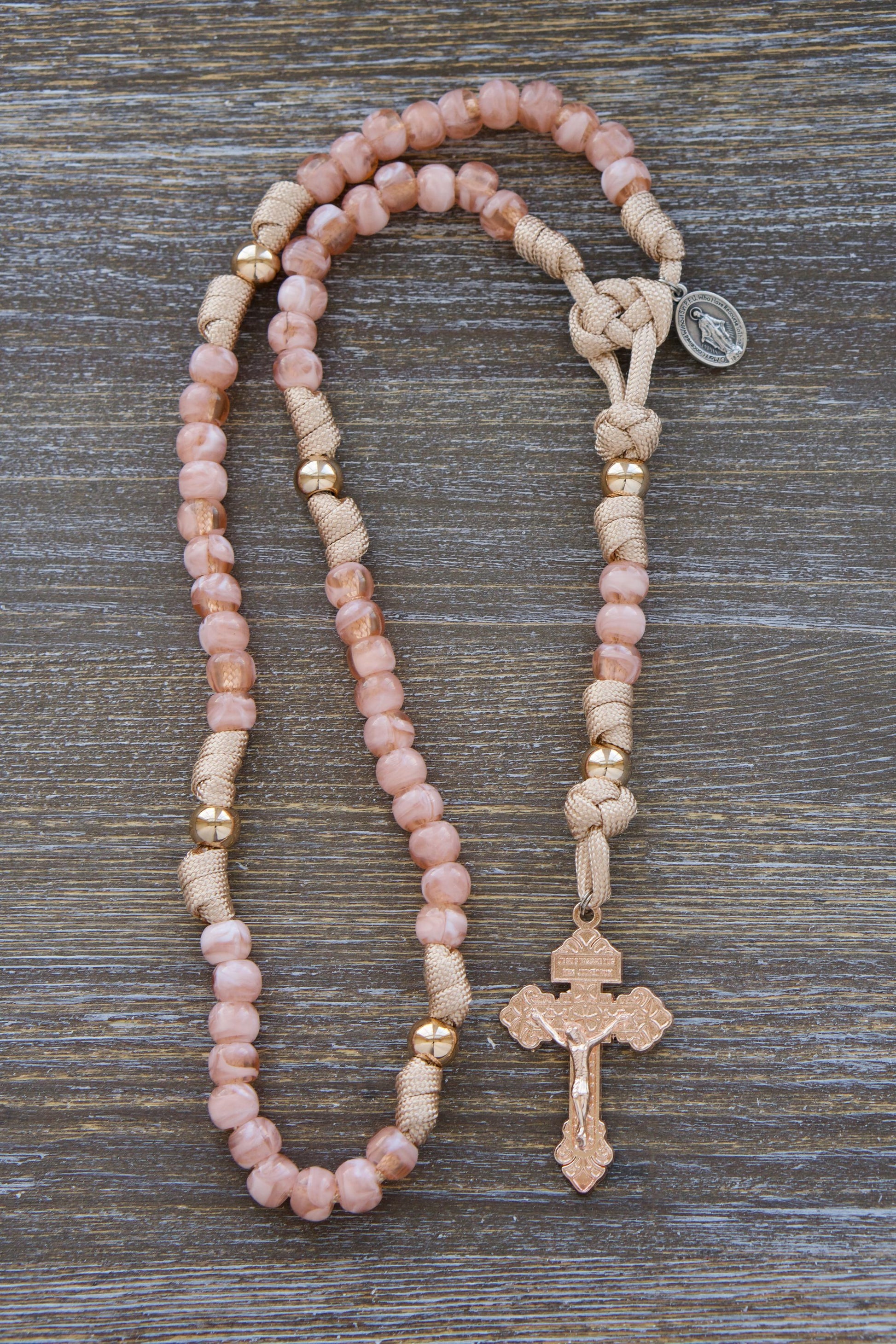 Vibrant rose-gold/tan paracord rosary designed for children, featuring milky pink Hail Mary beads and shiny gold Our Father beads. Includes a unique 2-inch rose gold Pardon Crucifix and smaller Miraculous Medal.