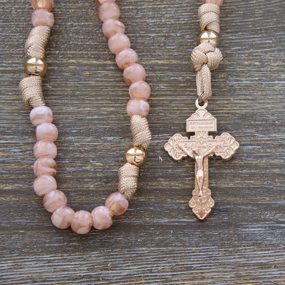 A child's paracord rosary named "Gate of Heaven", featuring rose gold/tan cord, milky pink Hail Mary beads, shiny gold Our Father beads, and a unique two-inch rose gold Pardon Crucifix. Includes a smaller Miraculous Medal devotional medal.