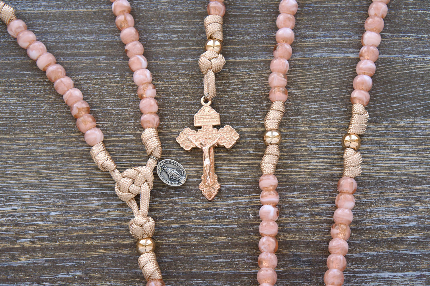 Kid's Paracord Rosary, 'Gate of Heaven' design. Features rose gold and tan paracord with milky pink Hail Mary beads and shiny gold Our Father beads. Includes a unique two-inch rose gold Pardon Crucifix and smaller Miraculous Medal devotional medal.