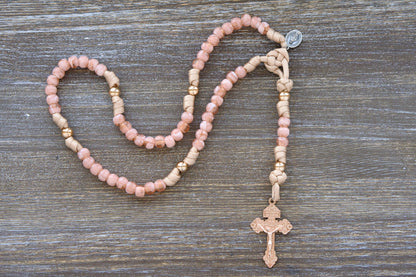 A child's paracord rosary, "The Gate of Heaven," features rose-gold and tan paracord interwoven with milky pink Hail Mary beads and shiny gold Our Father beads. It includes a unique two-inch rose-gold Pardon crucifix and a smaller Miraculous Medal devotional medal.