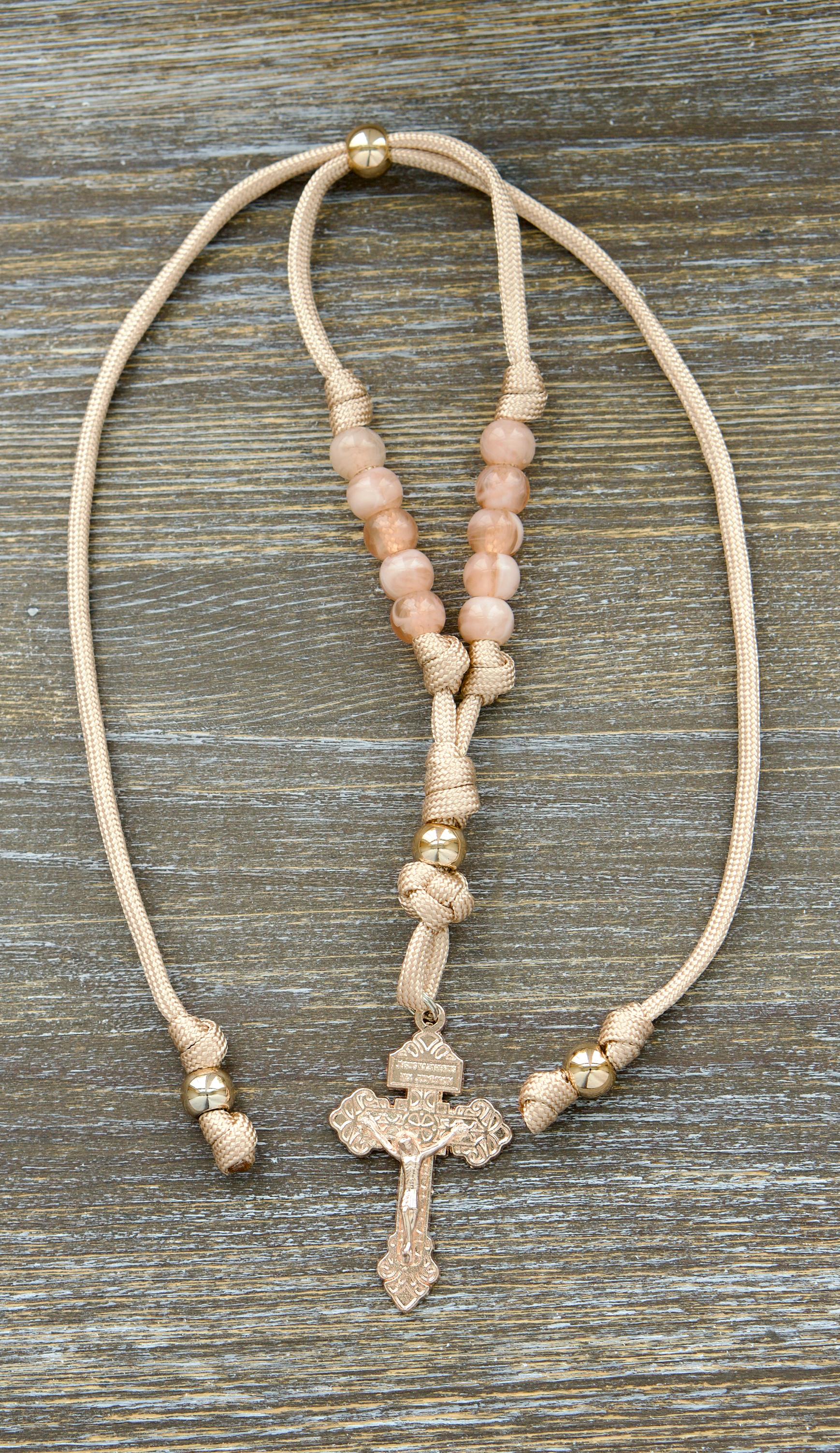 Gate of Heaven Rearview Mirror Rosary: A handcrafted tan and rose gold paracord rosary featuring milky pink Hail Mary beads, a striking rose gold Our Father bead, and an exclusive rose gold Pardon Crucifix.