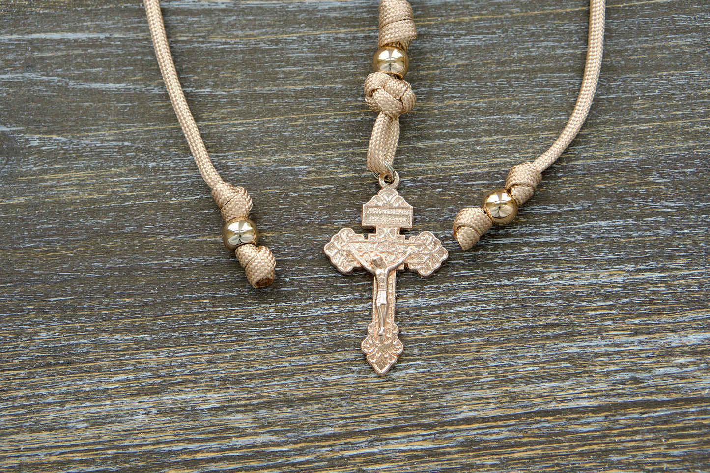 Tan and rose gold paracord rosary designed for rearview mirror hanging, featuring a unique rose gold Pardon crucifix centerpiece, milky pink Hail Mary beads, and a prominent rose gold Our Father bead.