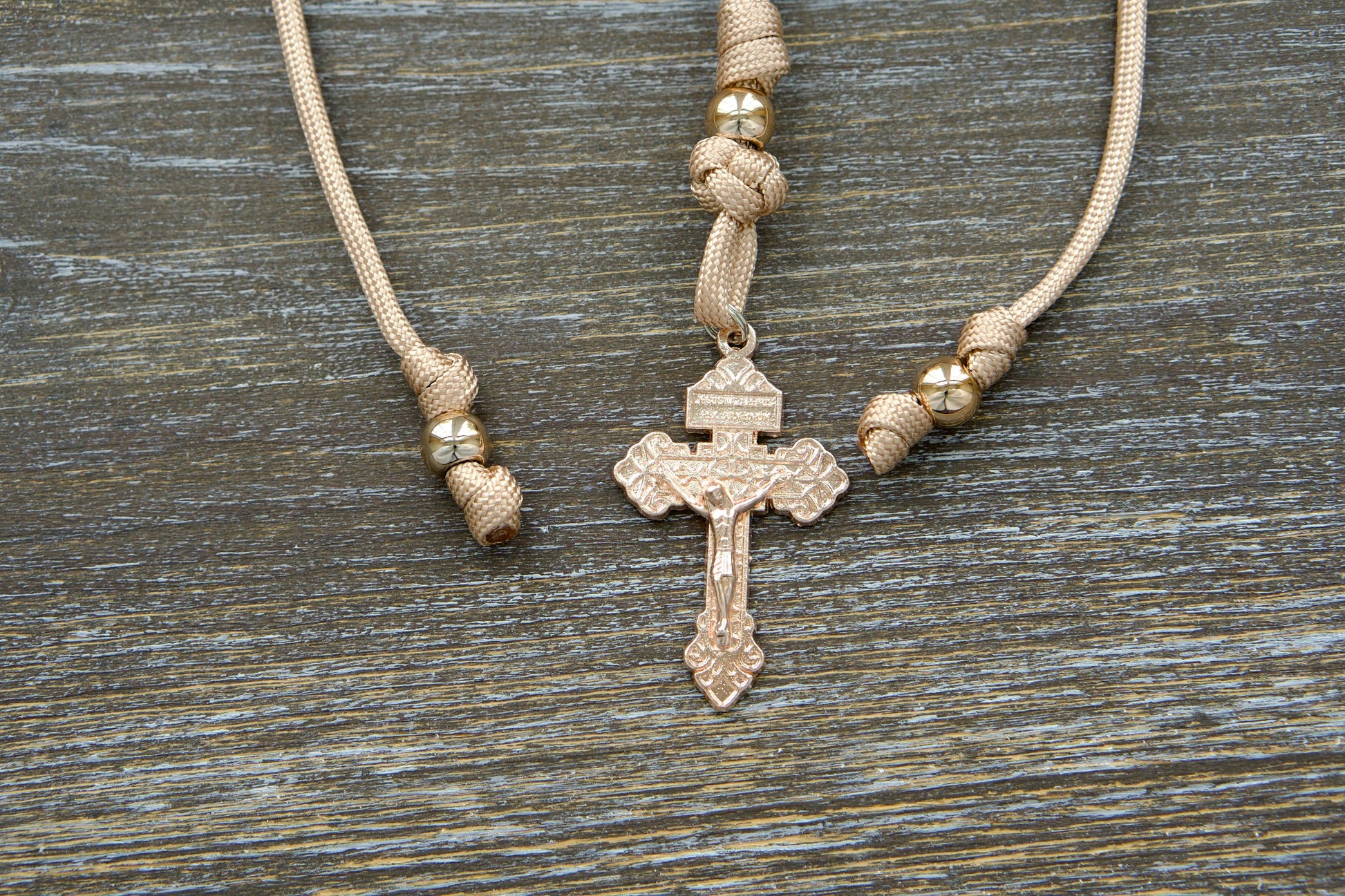 Tan and rose gold paracord rosary designed for rearview mirror hanging, featuring a unique rose gold Pardon crucifix centerpiece, milky pink Hail Mary beads, and a prominent rose gold Our Father bead.