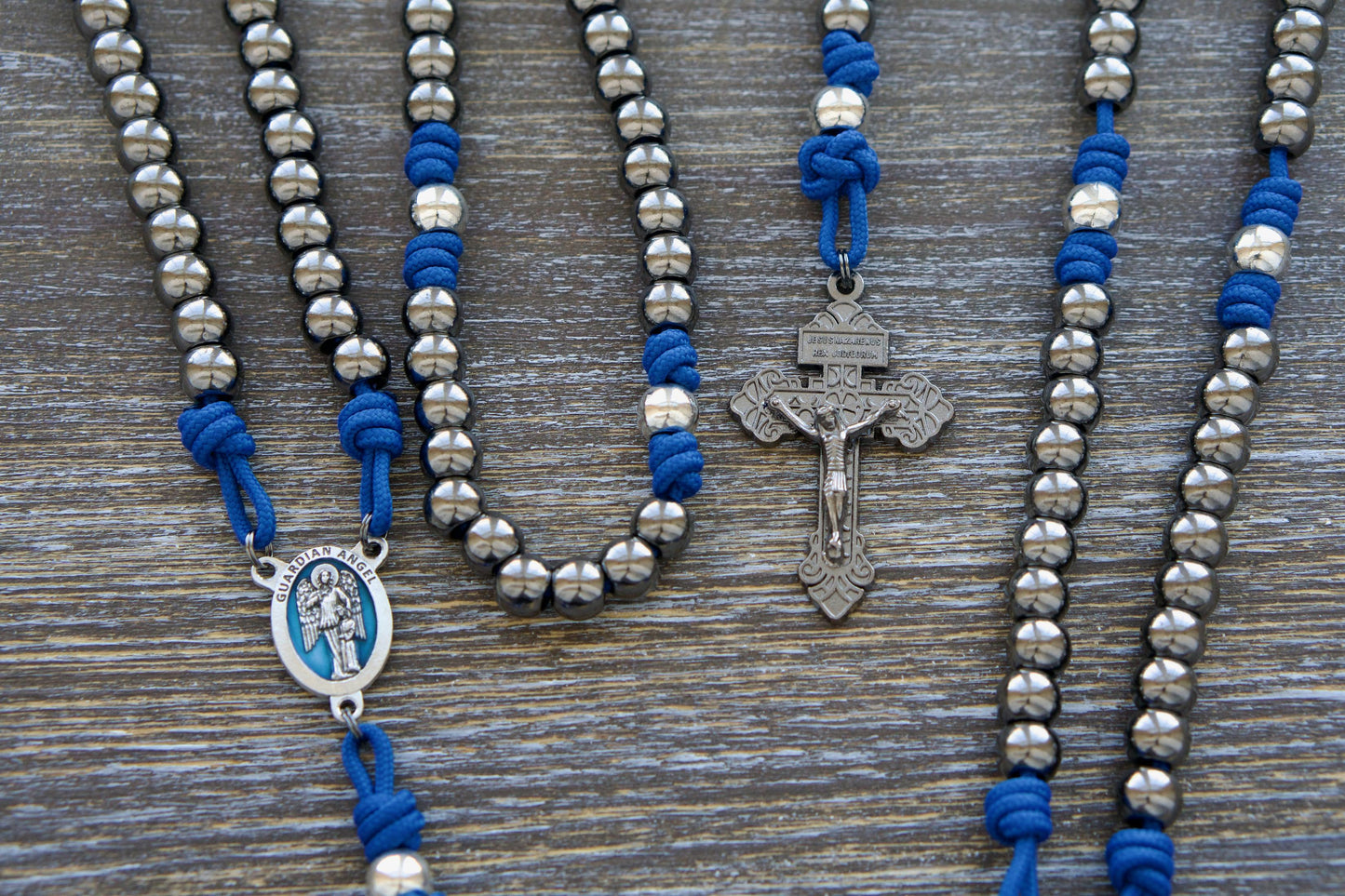 Guardian of Grace Rosary: A premium paracord rosary featuring a striking blue and silver design accented by a detailed blue enamel guardian angel centerpiece. Handcrafted for durability and devotion, it serves as a powerful reminder of God's constant protection.  