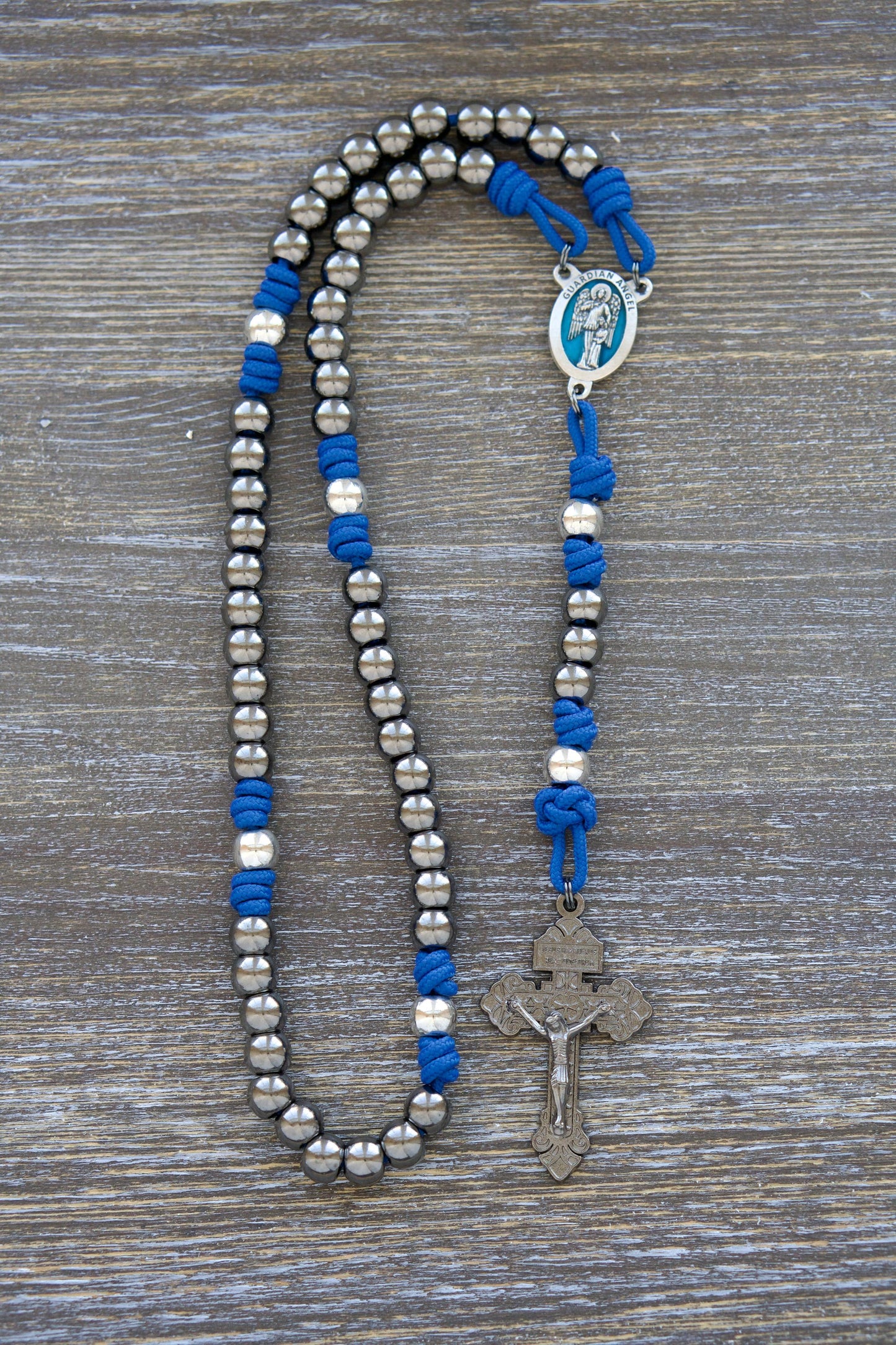 Premium metal paracord rosary featuring a stunning blue enamel Guardian Angel centerpiece. Durable royal blue paracord, gunmetal Hail Mary beads, and silver Our Father beads create an elegant devotional tool for enhancing prayer to your holy Guardian Angel.